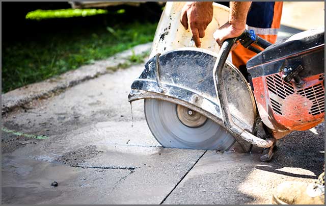 A construction worker cutting through asphalt with a diamond saw machine