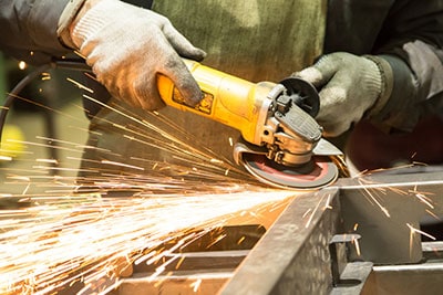 A worker cutting through metal with a hand-held angle grinder