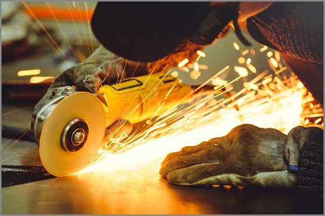 A worker cutting through hard material with a hand-held angle grinder