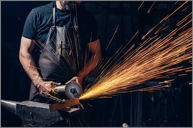 A worker using an angle grinder in a factory