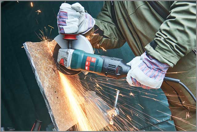 A worker cutting through a metal sheet with an angle grinder