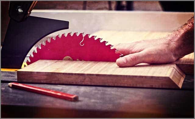 A human hand in a dangerous position close to a table saw blade