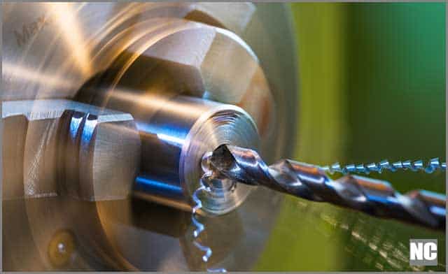 Close-up of a metallic workpiece clamped in a rotating machine chuck with steel twist drill bits