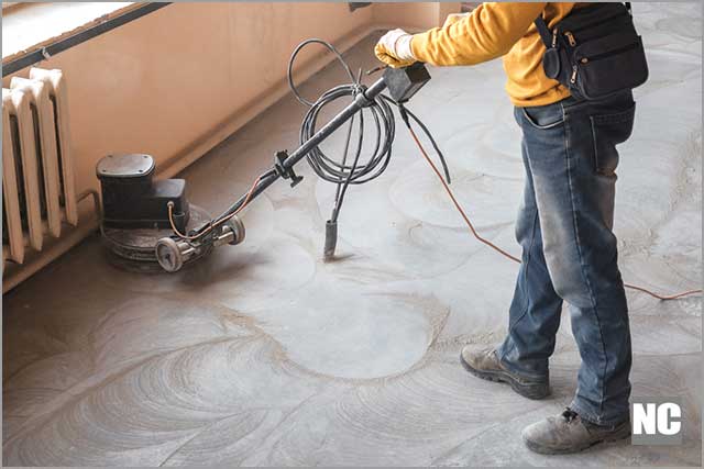A worker grinding concrete surface using a grinder with a diamond cup wheel