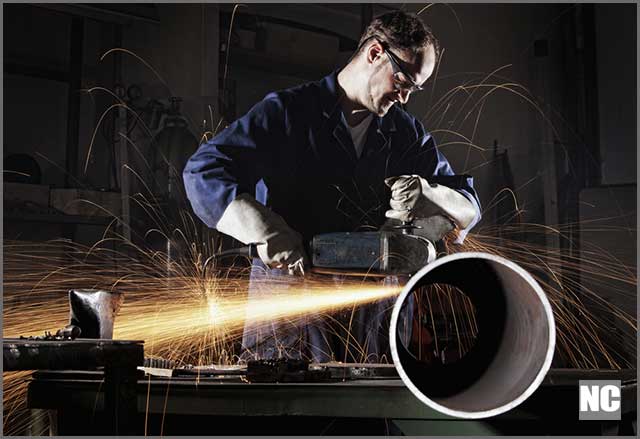 Heavy industry workers cut steel pipes with angle grinder in workshop