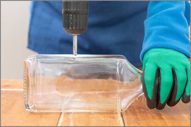 A person drills a hole in a glass bottle