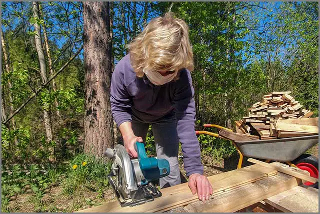 A masked woman using a circular blade to cut wood