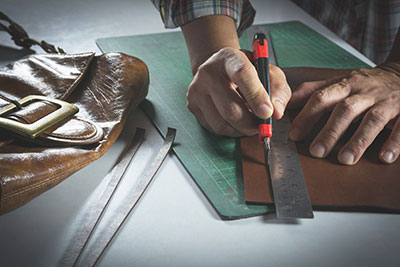A man is cutting a piece of leather with a knife.