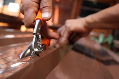 A worker is using a pair of scissors to cut through sheet metal.