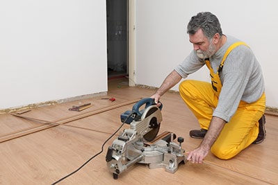 A worker is cutting a piece of wood for laminate flooring.