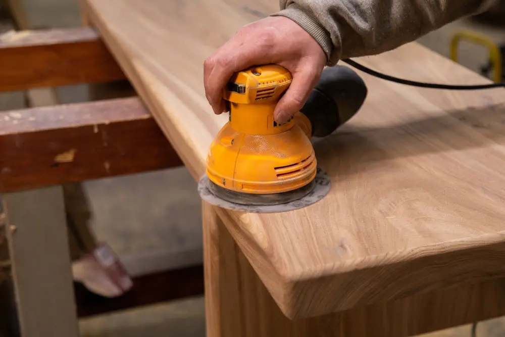 A carpenter is sanding wood with an orbital sander.